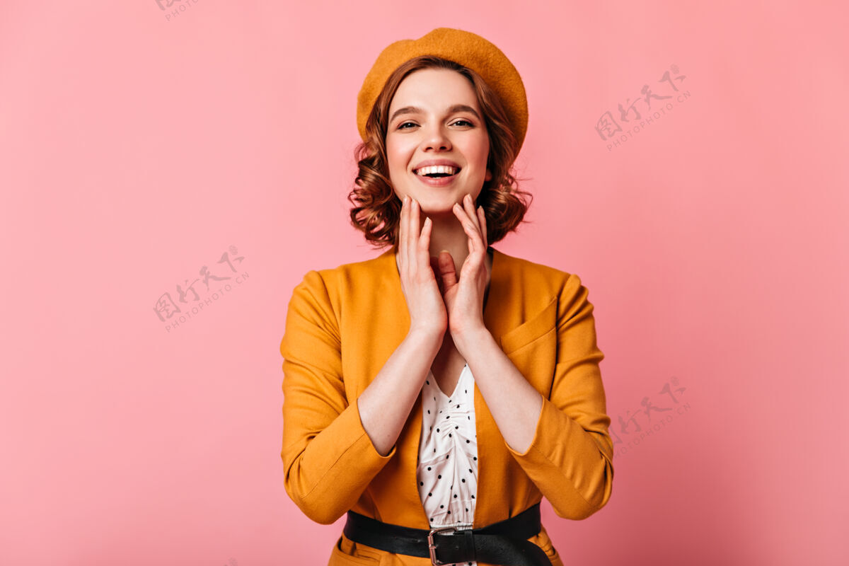 年轻黄色贝雷帽的可爱女人的正面图粉红色背景下微笑的卷发女孩的摄影棚照片女孩卷发法国