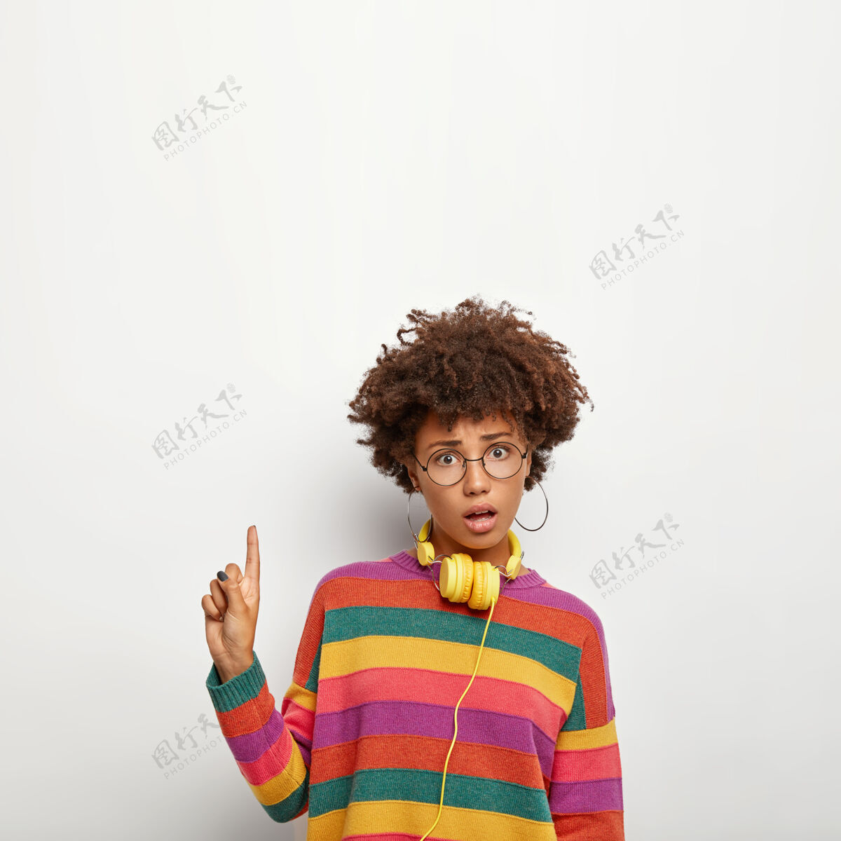 套头衫好奇不解的女人观察有趣的东西 用食指指着上面 为你的宣传片展示空间 戴着圆眼镜和彩色毛衣站人促销