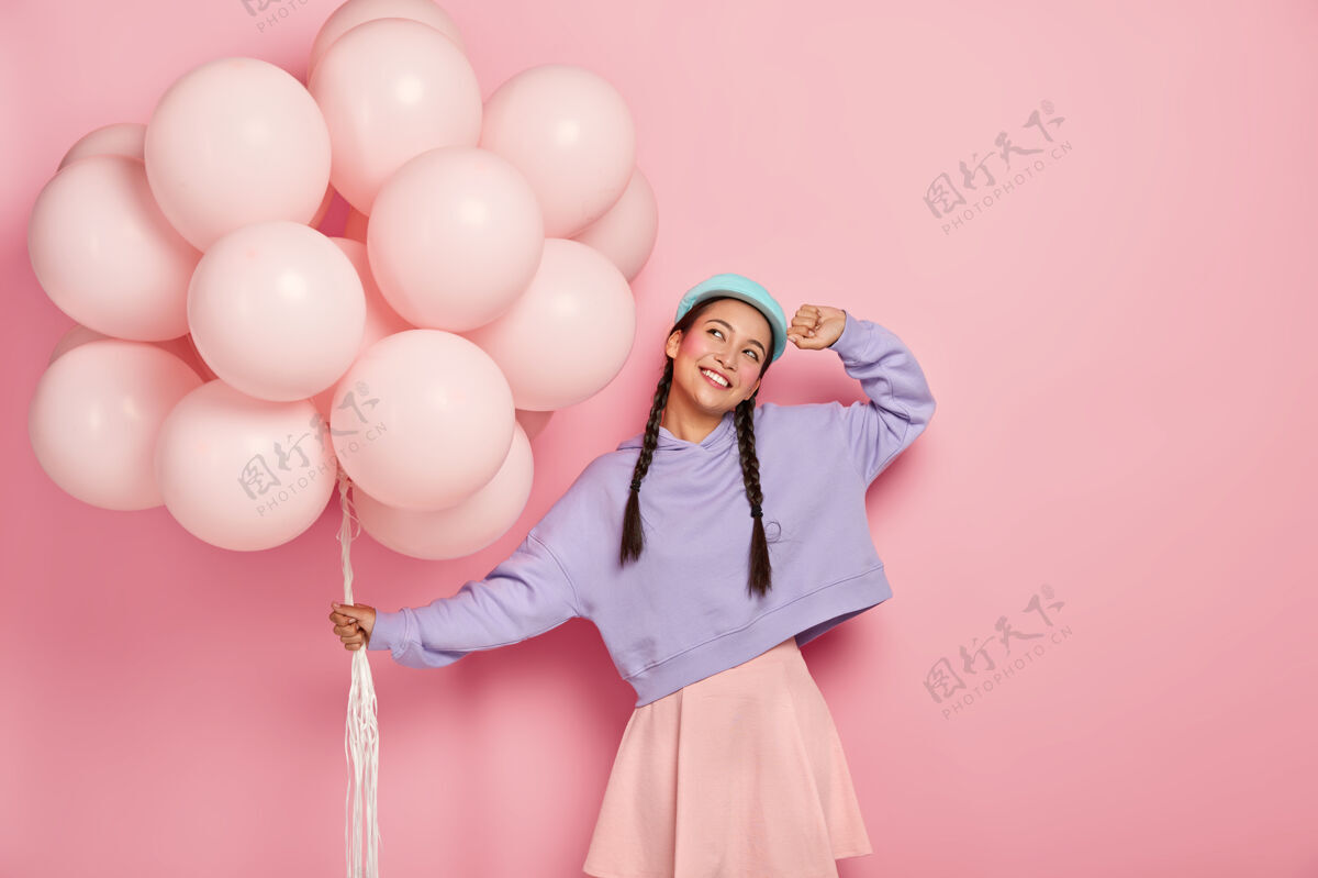 快乐快乐的亚洲年轻女子 梳着两条辫子 梦想着美好的节日 带着一堆气球 想象着美丽的庆祝时刻 孤立在粉红色的墙上束室内模特