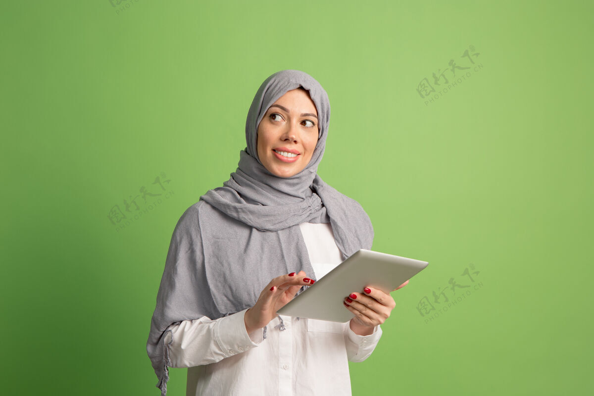女士戴着头巾的快乐阿拉伯女人拿着笔记本电脑微笑女孩的肖像 在绿色工作室摆姿势肖像女性欢乐