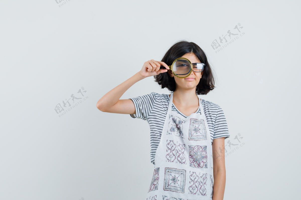女穿t恤 围裙的小女孩透过放大镜看着 看起来很懂事 积极童年玻璃