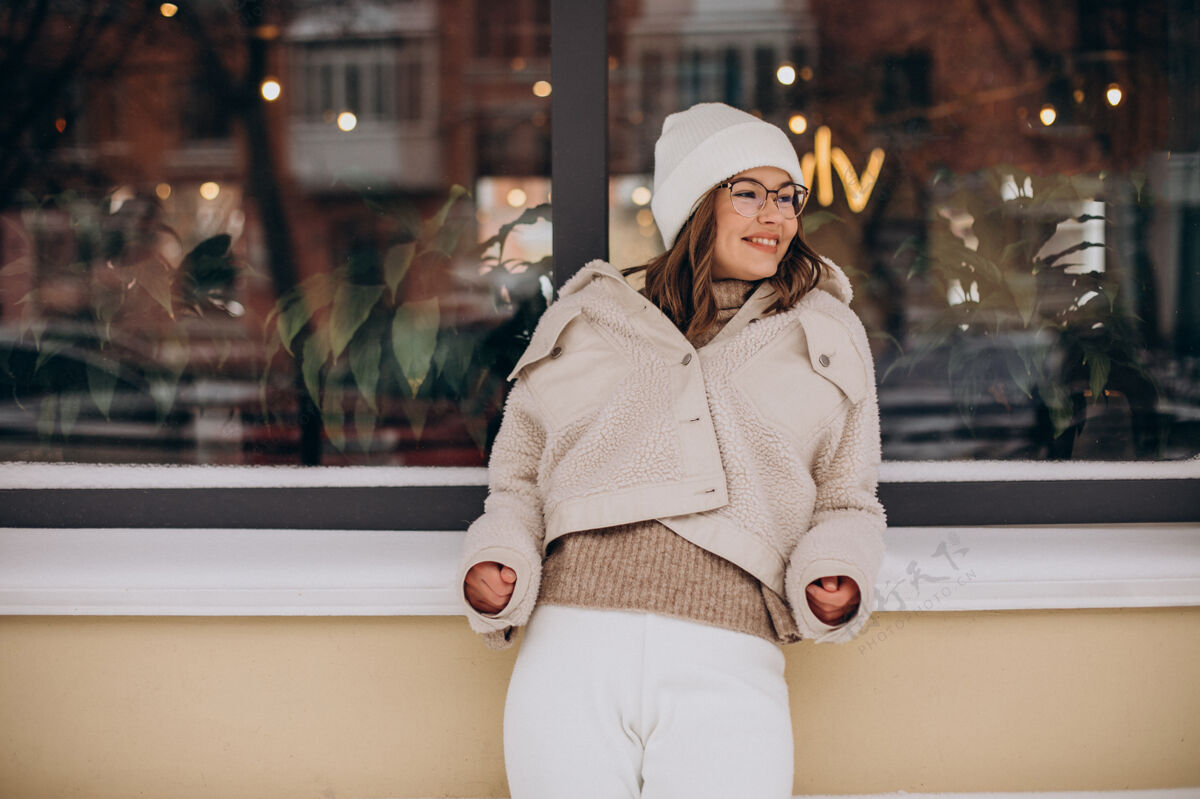 现代穿米色衣服的年轻漂亮女人在冬天走在街上微笑街头风格帽子