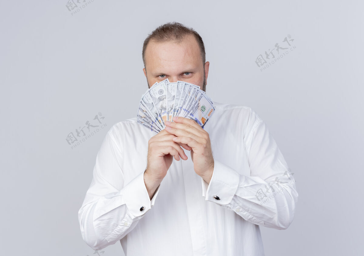 男人一个留着胡子 穿着白衬衫 手里拿着现金 狡猾地站在白墙上微笑的男人现金拿着微笑