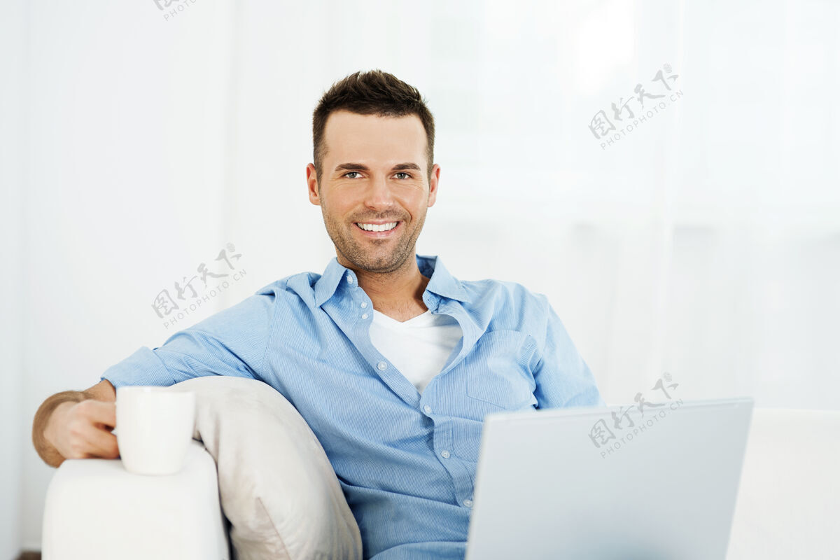 面部表情开朗的男人用笔记本电脑和咖啡放松枕头咖啡杯舒适