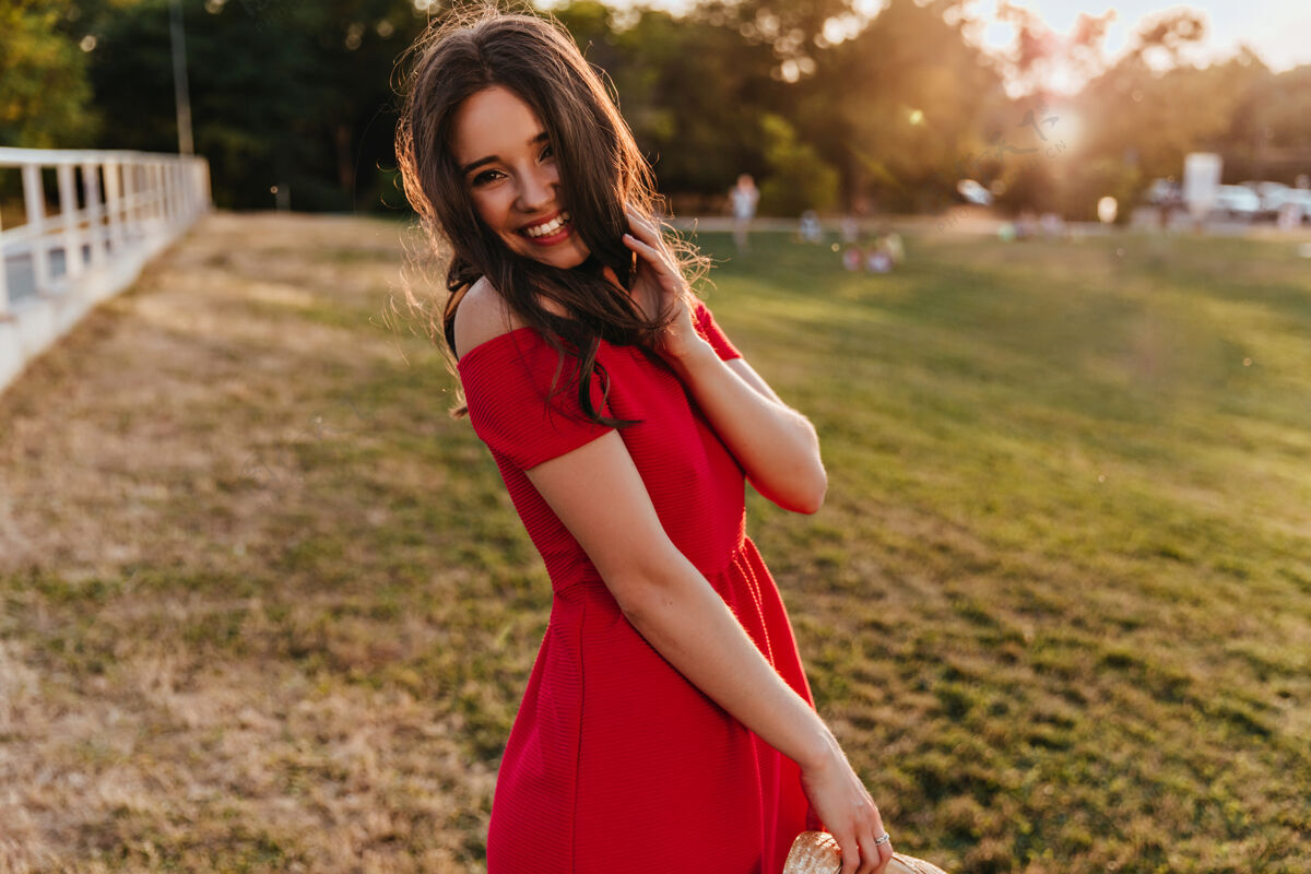 减肥在阳光明媚的日子里 穿着时髦的红色连衣裙的无忧无虑的女孩翩翩起舞盛夏盛装的热情黑发年轻女子在公园里令人心寒时尚深色服饰