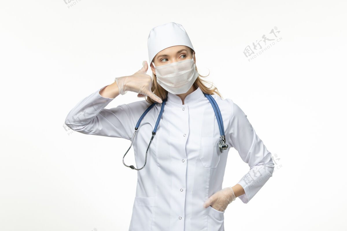 电话正面图女医生穿着医疗服戴着口罩和手套因冠状病毒打电话摆在白色办公桌上大流行冠状病毒大流行套装姿势