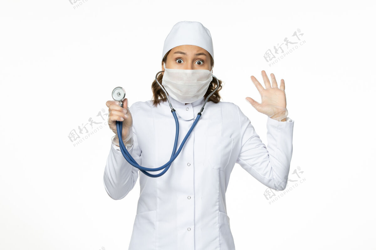 正面正面图女医生穿着白色医疗服 戴着口罩 在白墙上用听诊器给大流行病毒治病护士病毒制服