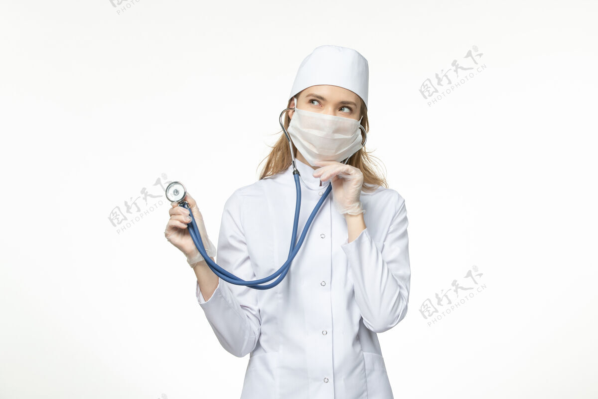 医疗正面图女医生穿着医疗服戴口罩因冠状病毒手持听诊器思考白墙病毒大流行-冠状病毒病冠状病毒防护正面冠状病毒预防