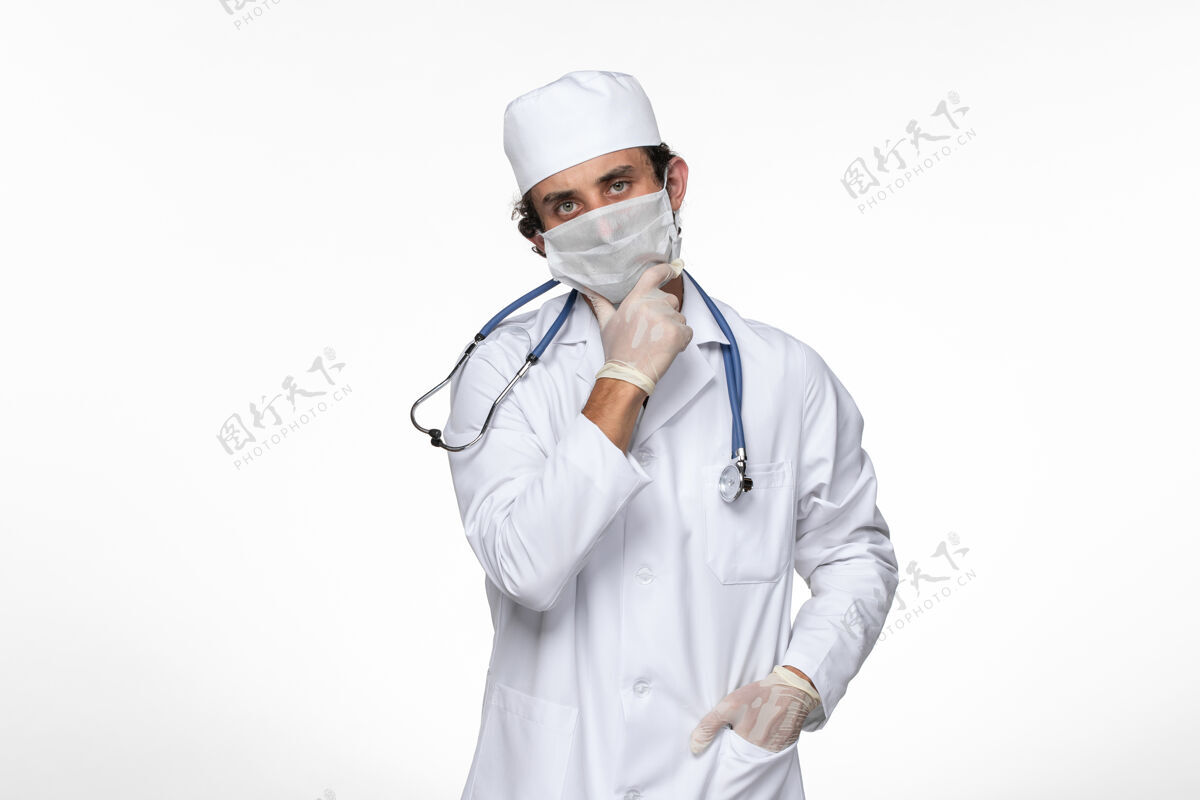 视图正面图男医生穿着医疗服戴无菌口罩以防病毒感染——思考白墙病毒病病毒大流行实验室外套穿着思考