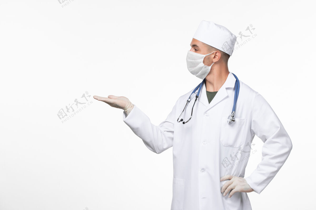 西装正面图：男医生穿着医疗服 戴着口罩 用听诊器对着白墙病毒冠状病毒-疾病大流行佩戴对抗专业