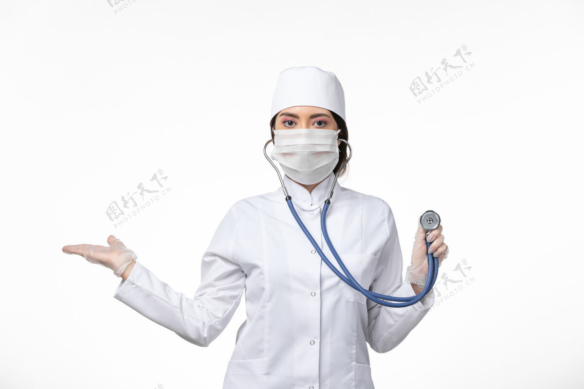 冠状病毒预防正面图女医生身穿白色无菌医疗服 戴口罩因冠状病毒-使用听诊器对白色地板进行病毒冠状病毒-大流行性疾病正面使用医生