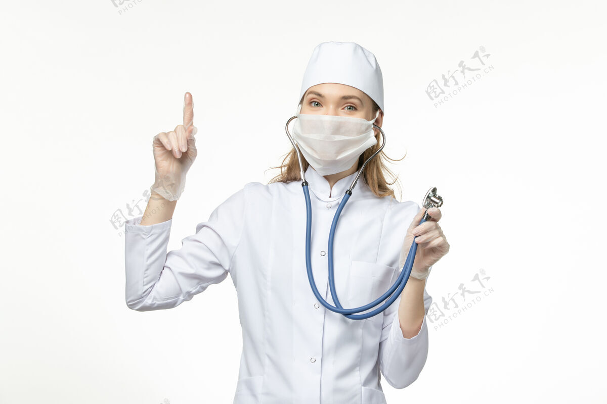 使用前视图穿着白色医疗服的女医生在白墙上使用听诊器疾病冠状病毒-大流行疾病人员医生疾病