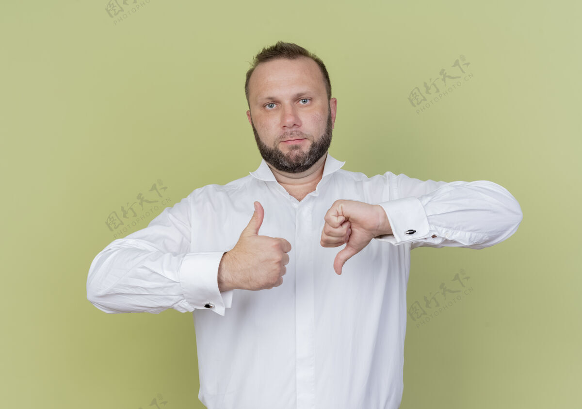 站一个留着胡子的男人穿着白衬衫 大拇指上下竖立在轻质的墙上穿男人胡须