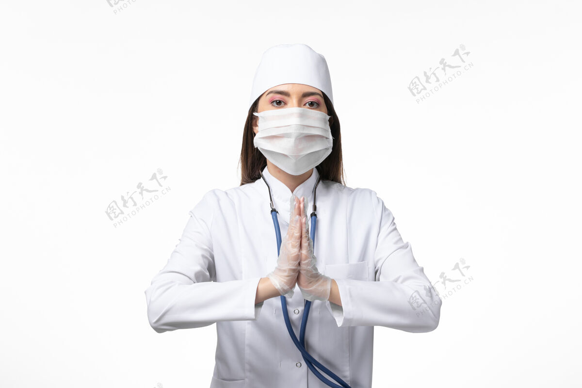 冠状病毒预防正面图女医生穿着白色无菌医疗服带口罩因冠状病毒祈祷白墙疾病冠状病毒-大流行病毒病视图专业祈祷