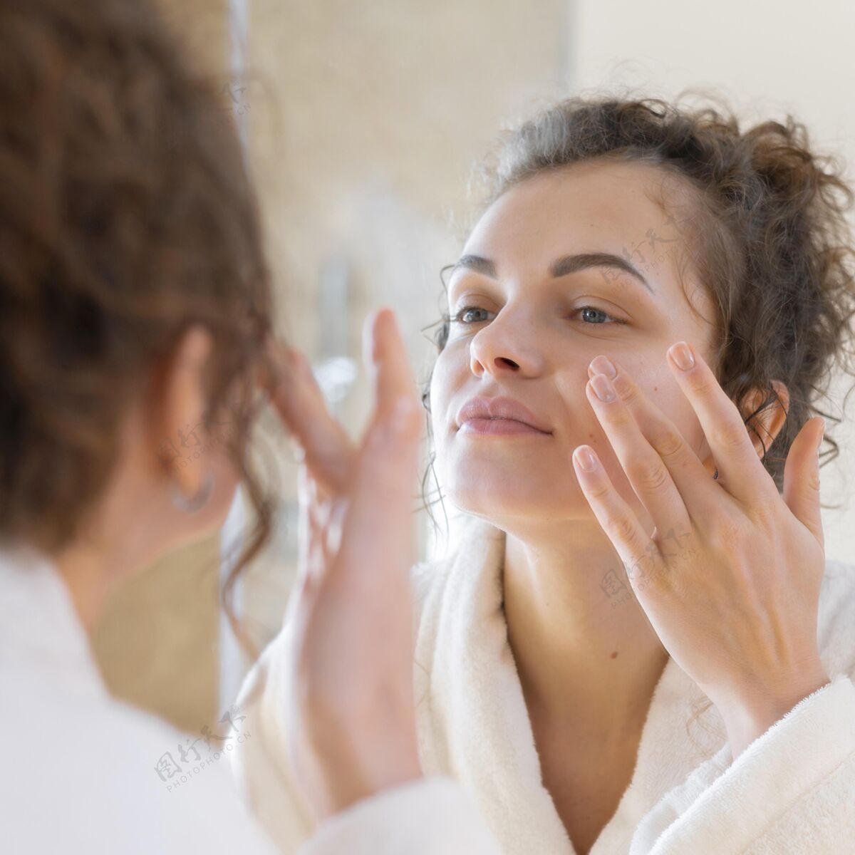 模特照镜子的时候在脸上涂面霜的女人面部护理自我护理室内