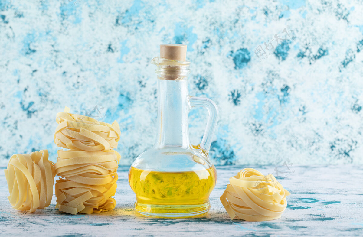 生的一堆塔格利亚特尔巢穴和一杯橄榄油在蓝色上烹饪干的意大利菜