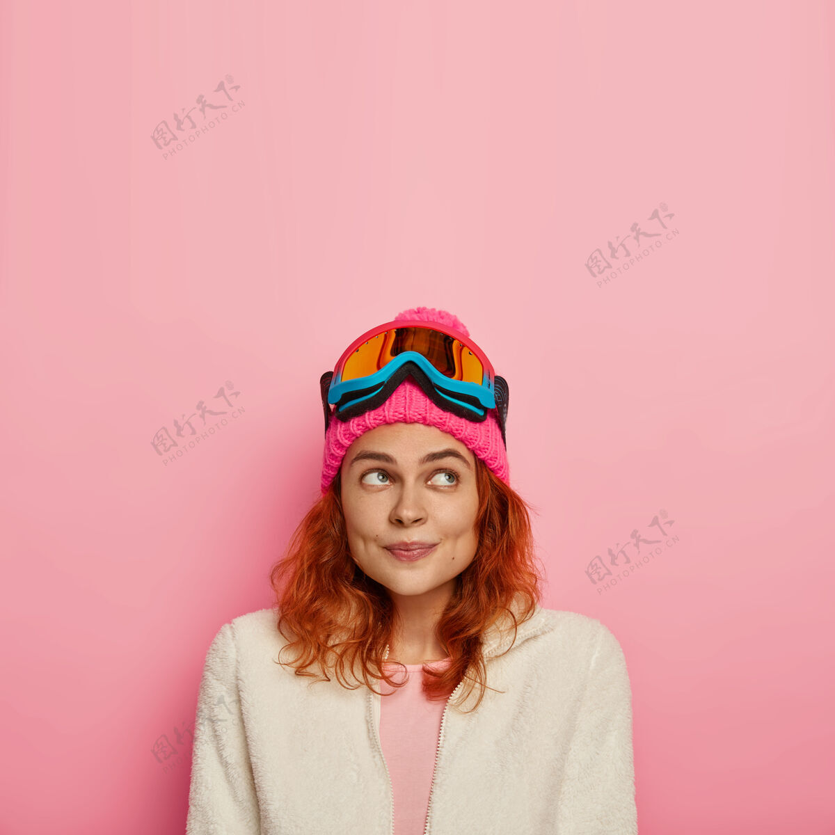 粉色垂直形象的快乐沉思的女旅行者穿着滑雪板 有着红色的头发 聚焦在上面 孤立在玫瑰色的墙上红发室内红发