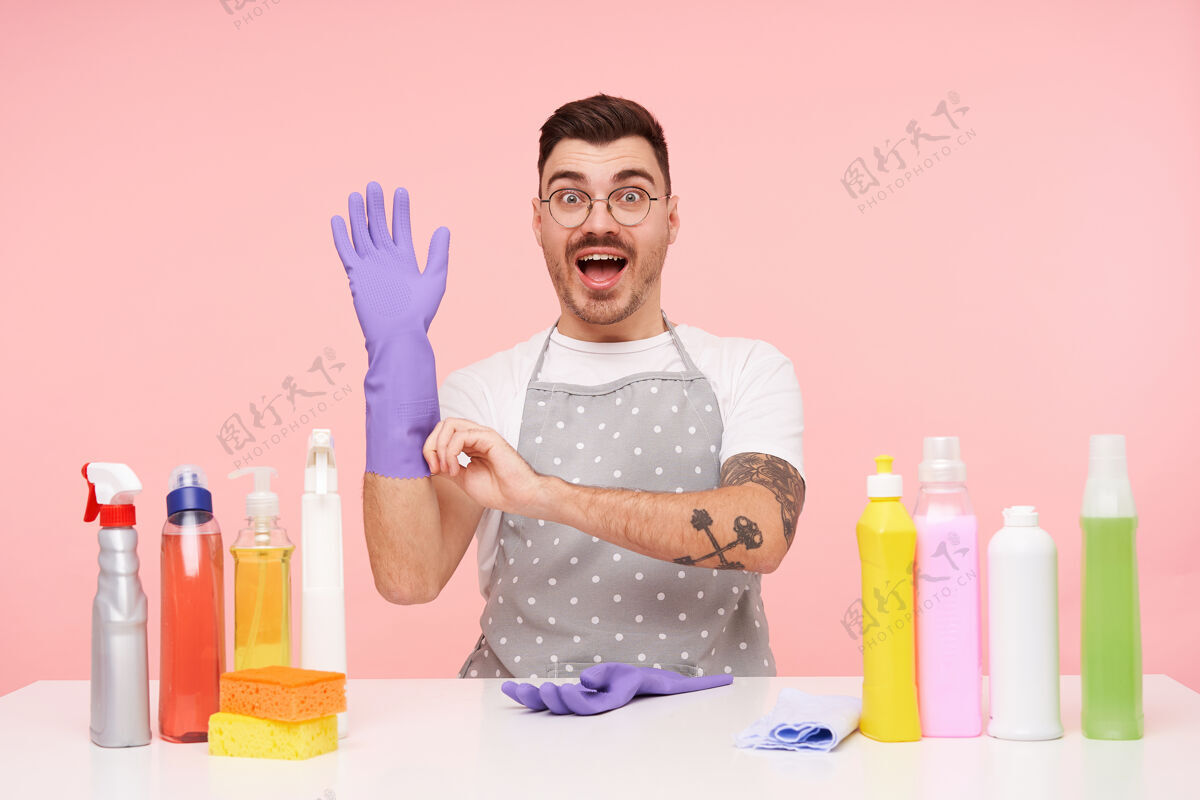 眼镜激动的年轻漂亮纹身黑发男子举起手在橡胶手套男士洗涤剂制服