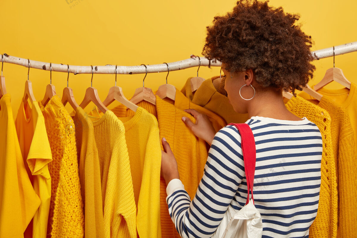 悬挂卷发女士穿着条纹套头衫 背着包 挑选衣服 拿起衣架上的黄色毛衣条纹零售套头衫