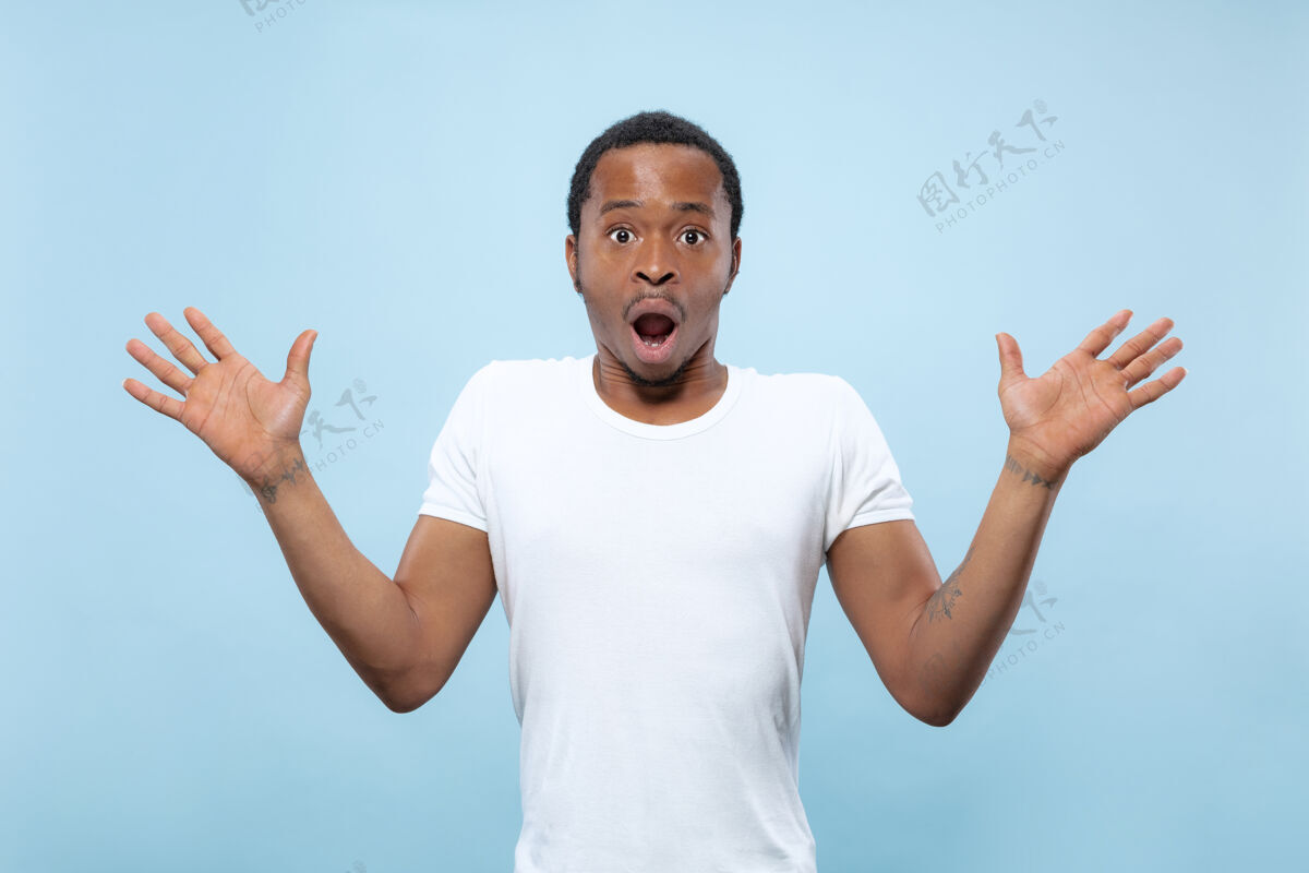男性半身特写肖像的年轻非洲裔美国男子在白色衬衫的蓝色空间人类的情感 面部表情 广告 销售理念邀请 看起来震惊和惊讶商人惊讶一半