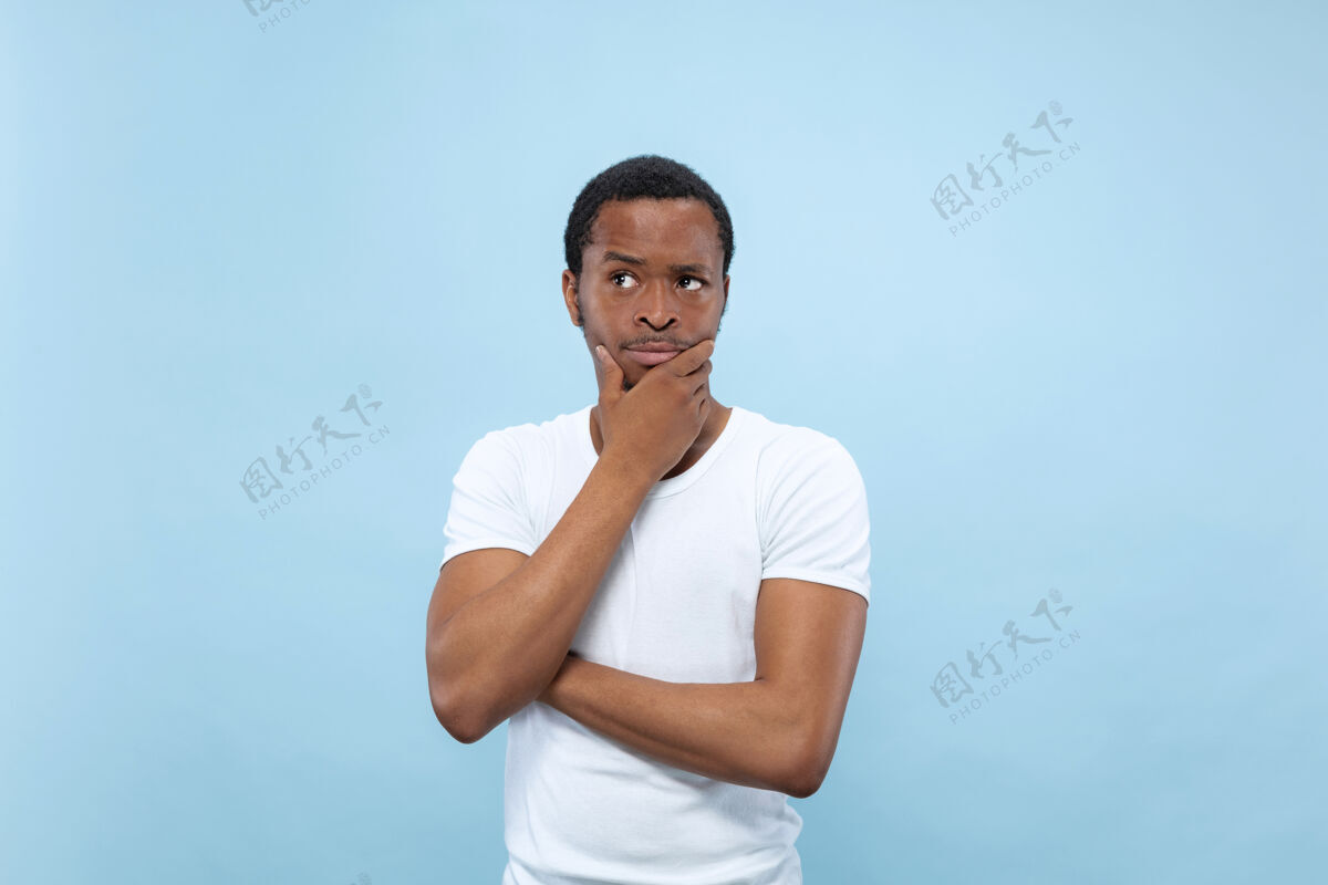 顺序半身特写肖像的年轻非洲裔美国男子在白色衬衫的蓝色空间人类的情感 面部表情 广告概念思想广告思考