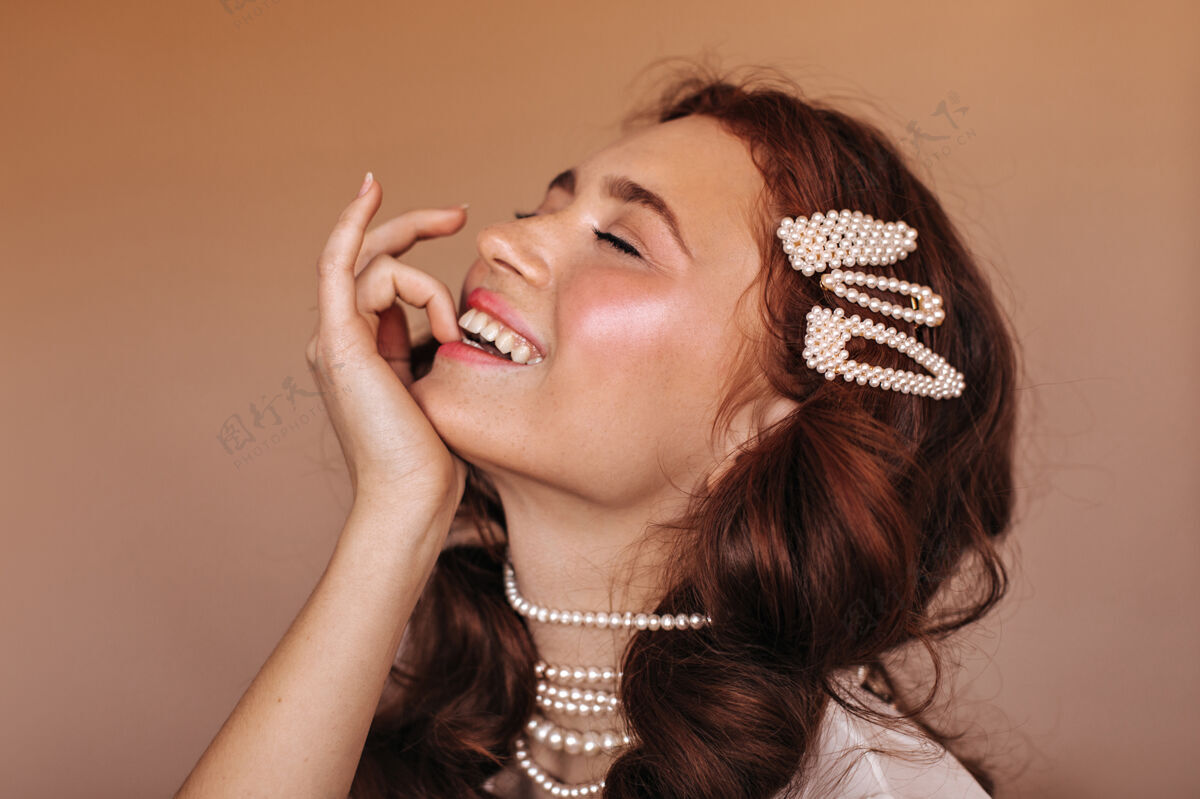 女士积极的卷发女人笑着咬着她的手指白色发夹和珍珠项链女人的肖像年轻漂亮女性化
