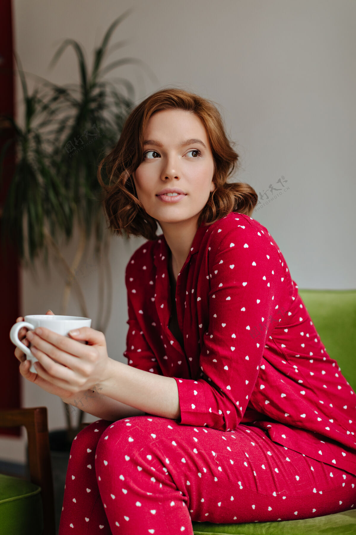 房子梦幻般卷曲的女人端着咖啡 望着别处室内拍摄的是穿着红色睡衣的快乐年轻女士喝茶的镜头复制空间茶卷发