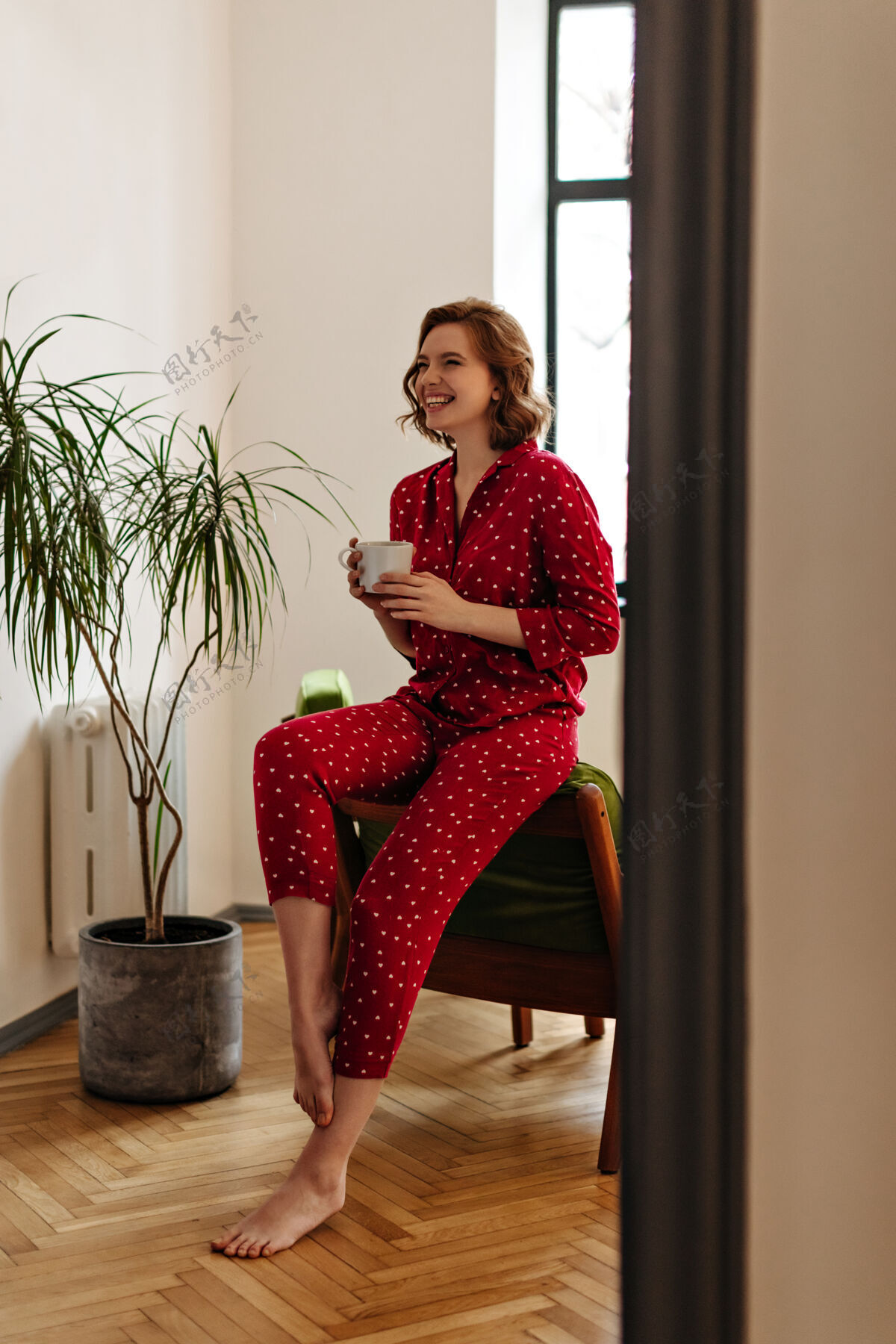 花光着脚笑着拿着咖啡的女人的全貌穿着红色睡衣的幸福女人在家里摆着姿势欢乐茶咖啡