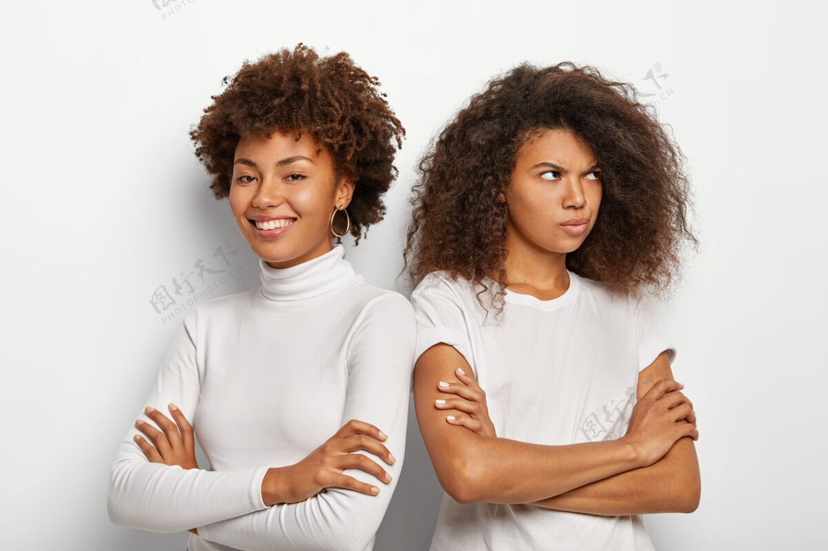 高兴不满的非洲女人从朋友身边转过身来 挽着胳膊 穿着休闲装 在白色背景下摆姿势两姐妹有误会团结手臂站