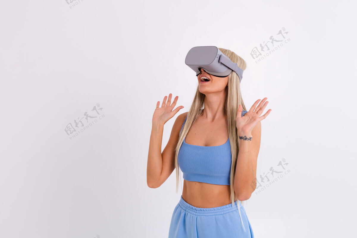 休闲摄影棚照片中一个年轻迷人的女子穿着温暖的蓝色时尚西装 戴着虚拟现实眼镜在白色的现实女性设备