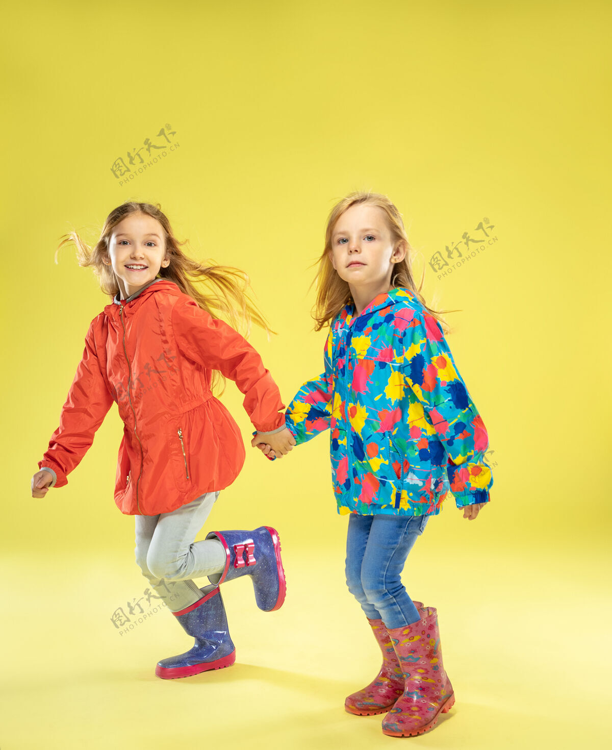 休闲黄色的画室墙上 一个穿着雨衣 手牵着手 奔跑着 玩得很开心的时髦女孩的完整肖像明亮童年春天