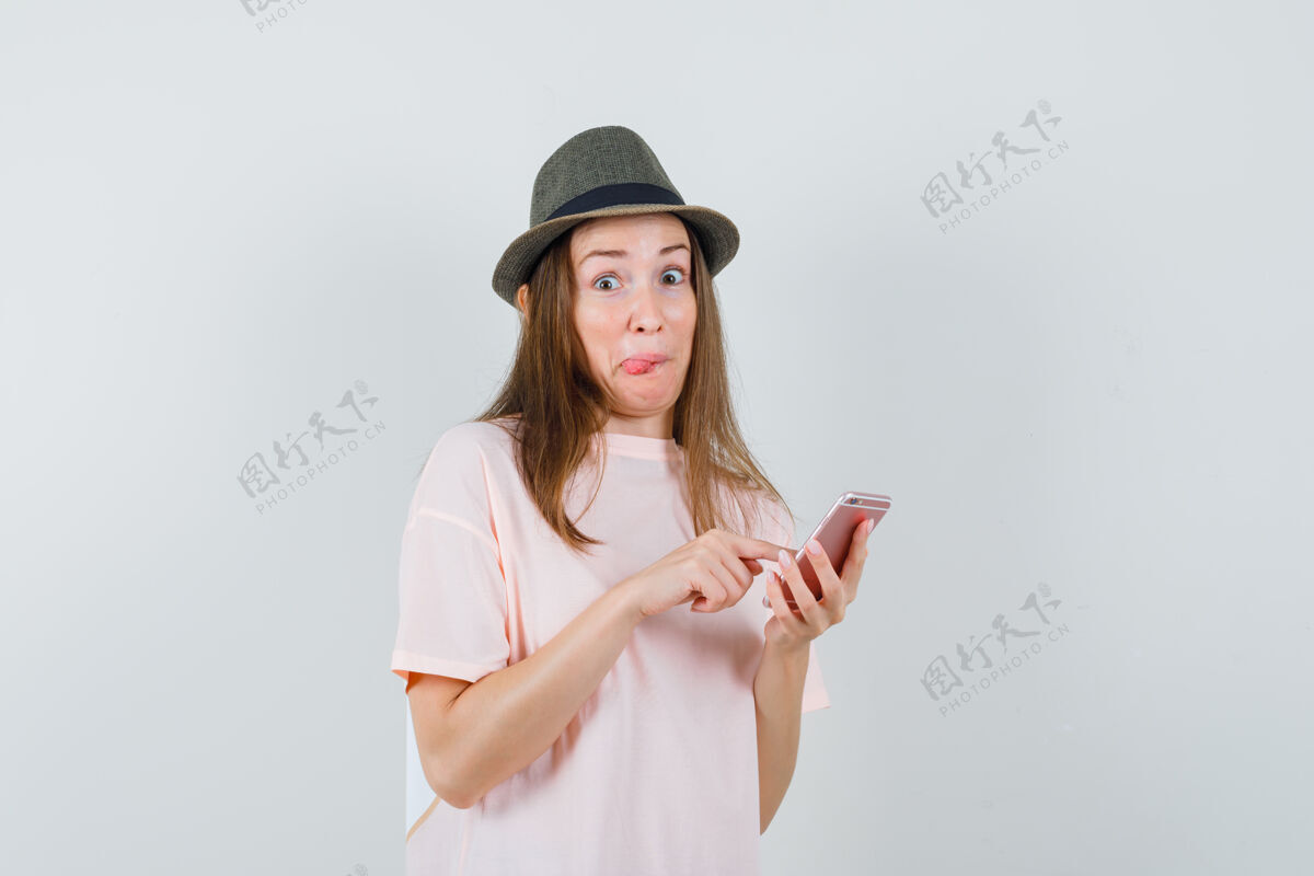 女人年轻女孩用手机穿着粉色t恤 戴着帽子 看上去很好奇前视图帽子快乐手机