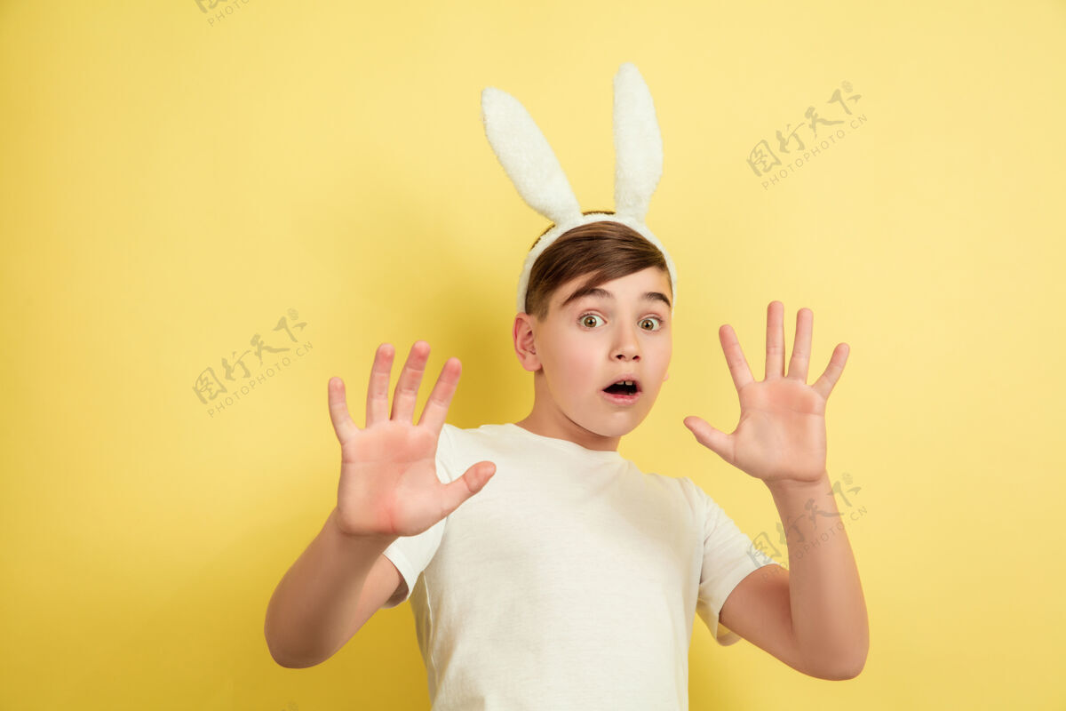 面部害怕 震惊白人男孩作为一个复活节兔子在黄色的工作室背景复活节快乐的问候肖像五颜六色表情
