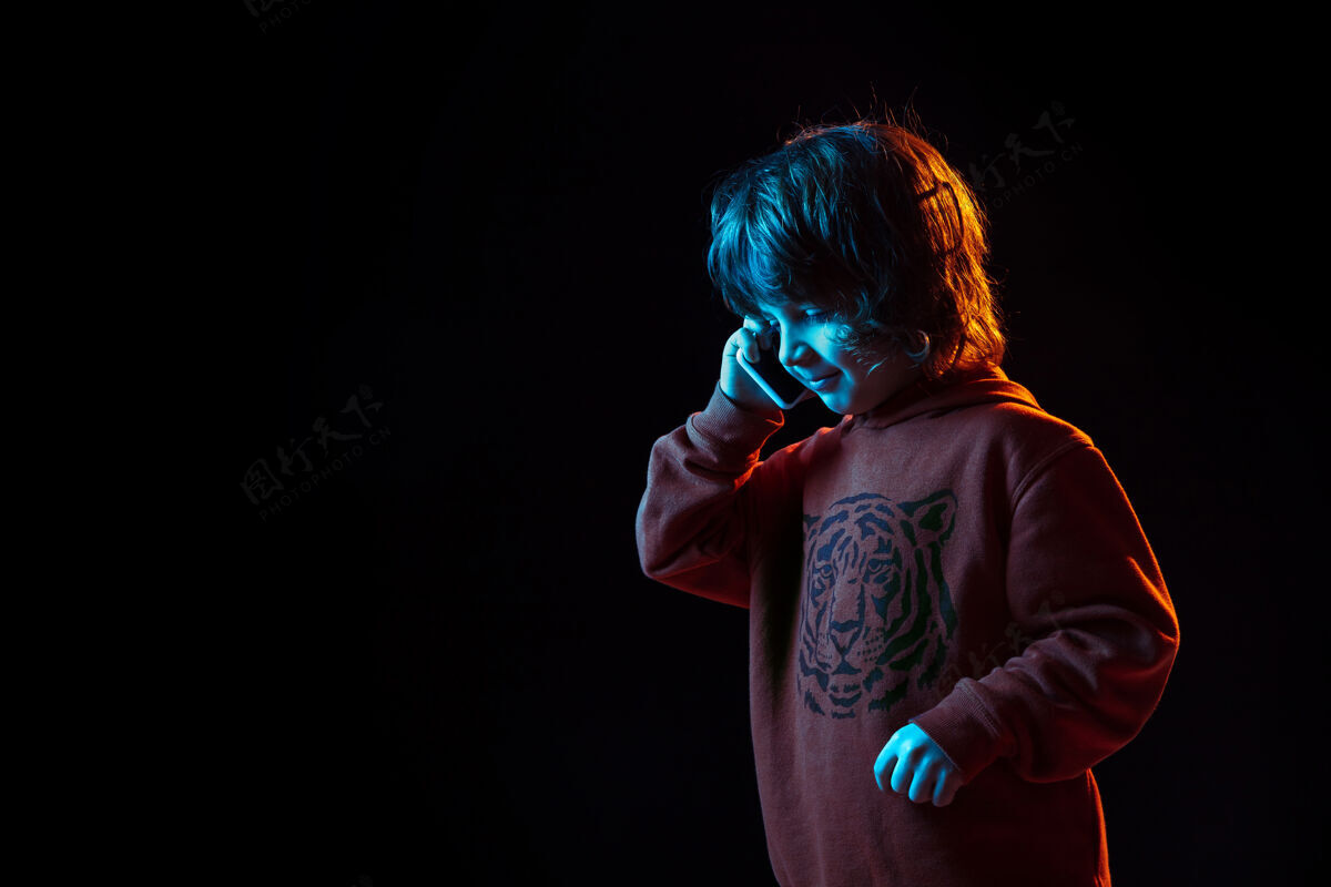 面部可爱的电话交谈在霓虹灯下的黑暗工作室背景上的白人男孩肖像美丽的卷曲模型情绪手机年轻