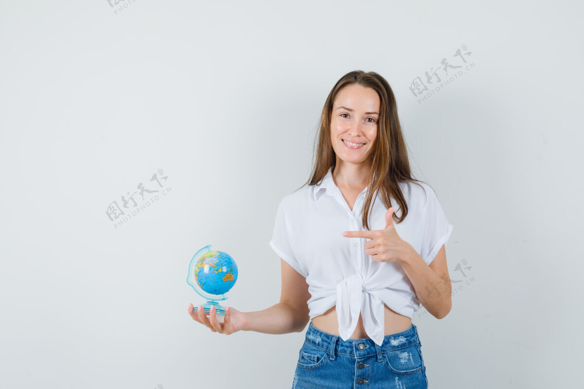 地球仪美丽的女士在白色衬衫指着迷你地球仪 前视图指向快乐优雅