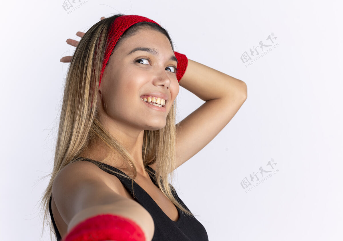 微笑身穿黑色运动服 头戴红色头巾的年轻健身女孩站在白色的墙壁上欢快地微笑着欢呼女孩健康