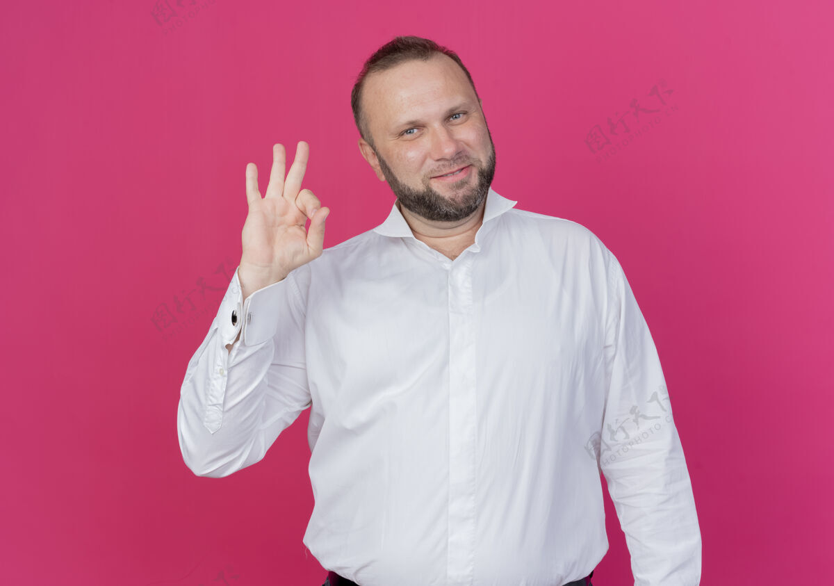 穿一个留着胡子的男人穿着白衬衫 站在粉色的墙上微笑着 看上去很好男人胡子站