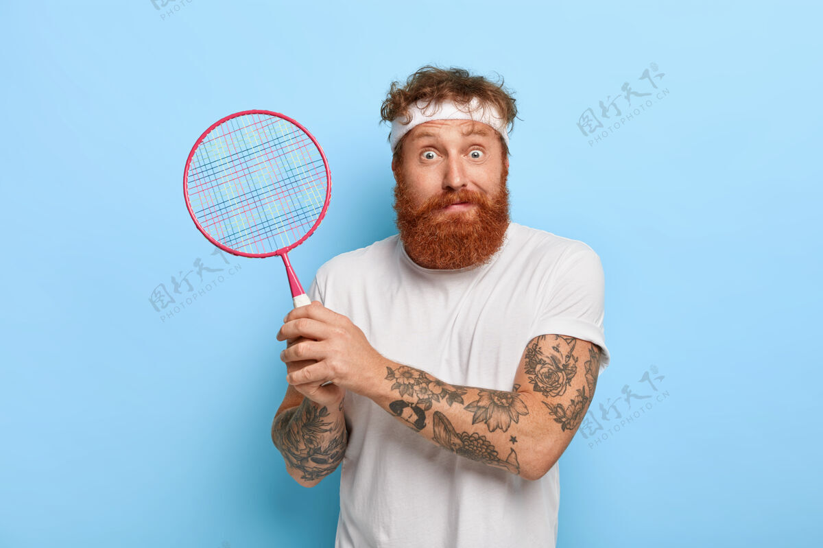 人红头发的网球运动员拿着球拍对着蓝色的墙壁摆姿势人运动红发