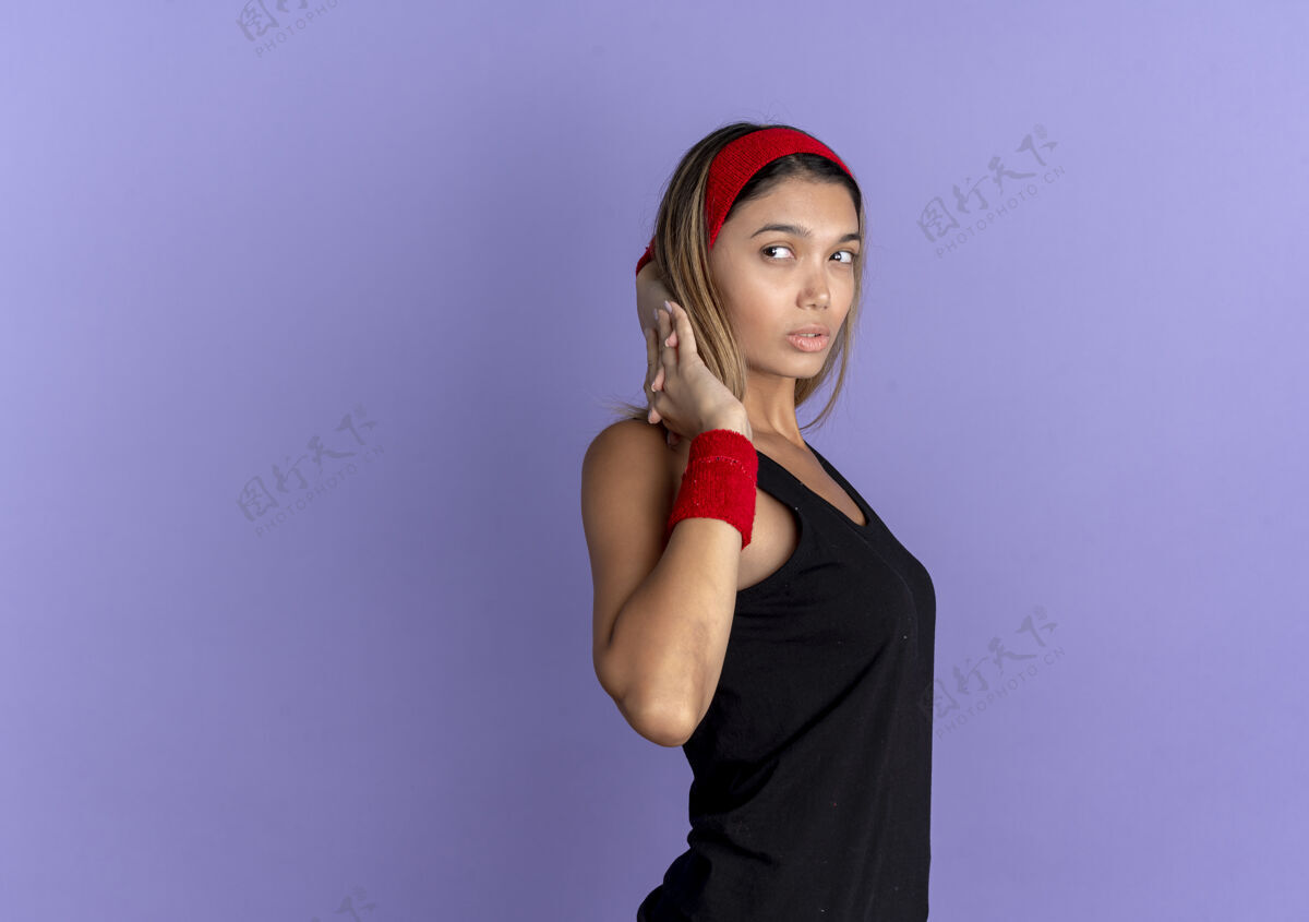 运动装身穿黑色运动服 头戴红色头巾的年轻健身女孩自信地站在蓝色的墙上伸展着身体健康头带她自己