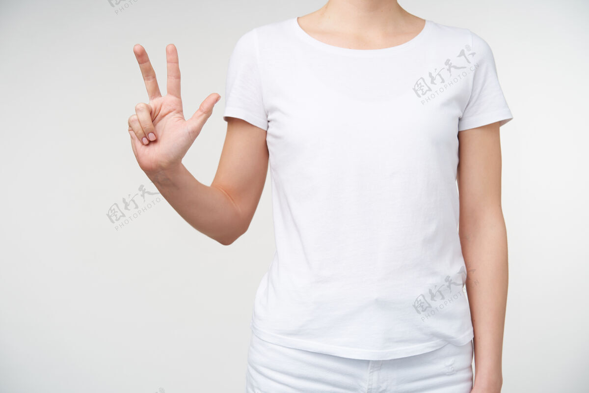 室内一张穿着休闲服的年轻女士站在白色背景上数着三个手指的室内照片人手和手势的概念年轻图形符号