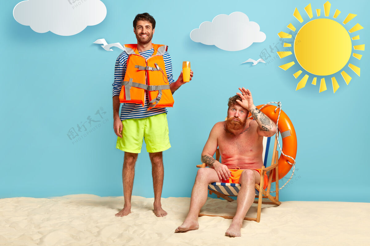 男性快乐的救生员和被晒伤的家伙在海滩上摆姿势男人防晒霜短裤