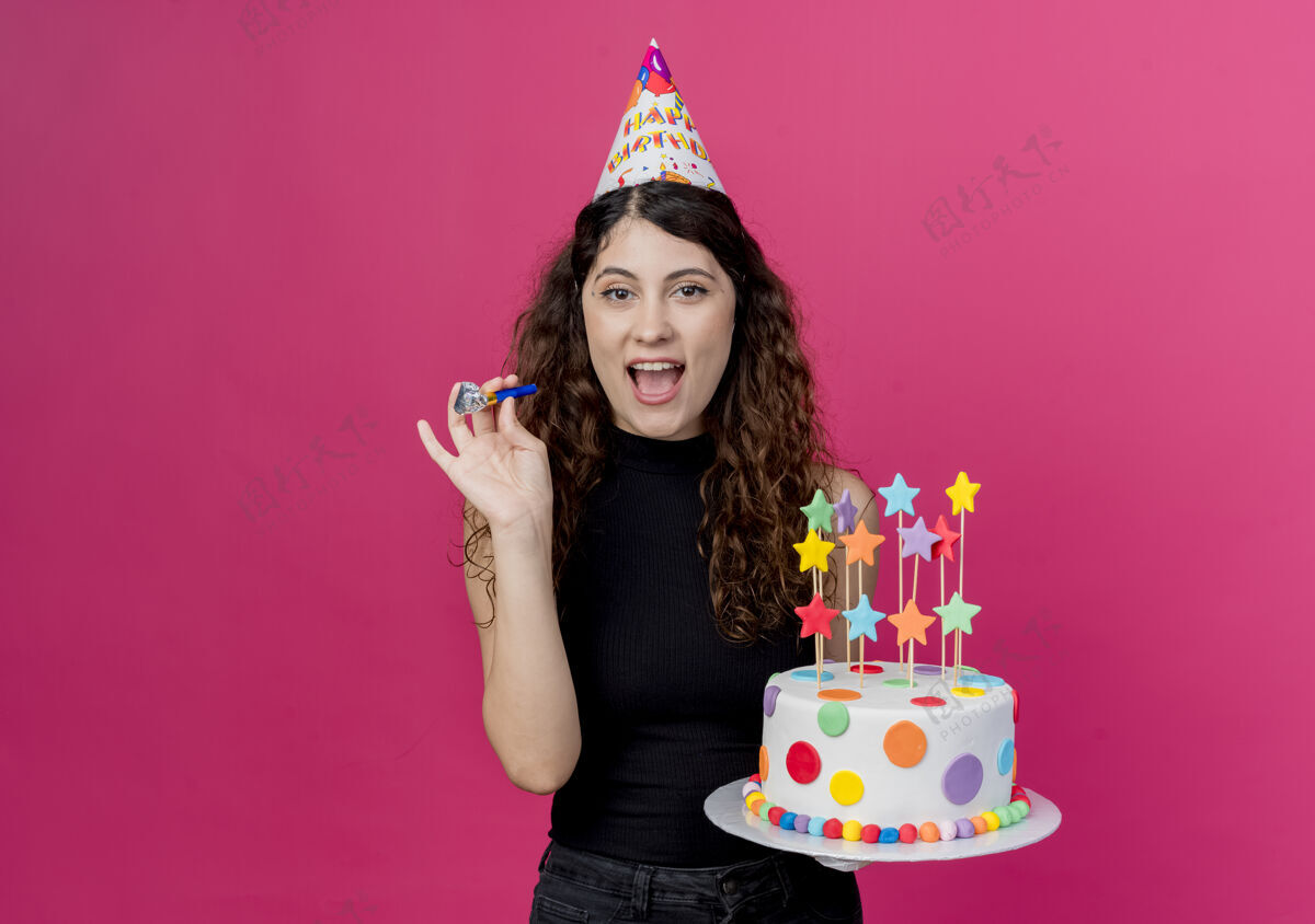 欢呼一位年轻漂亮的女士 卷发 戴着节日帽 手里拿着生日蛋糕 高兴而兴奋地微笑着 站在粉色的墙上 高高兴兴地庆祝生日兴奋抱着卷发