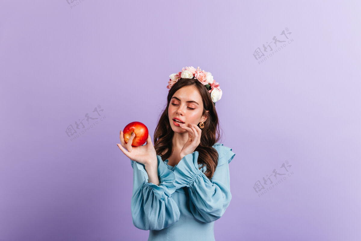 表情心情很好的女孩正看着美味的红苹果隔着墙的蓝色女衬衫的快照女人人欢呼