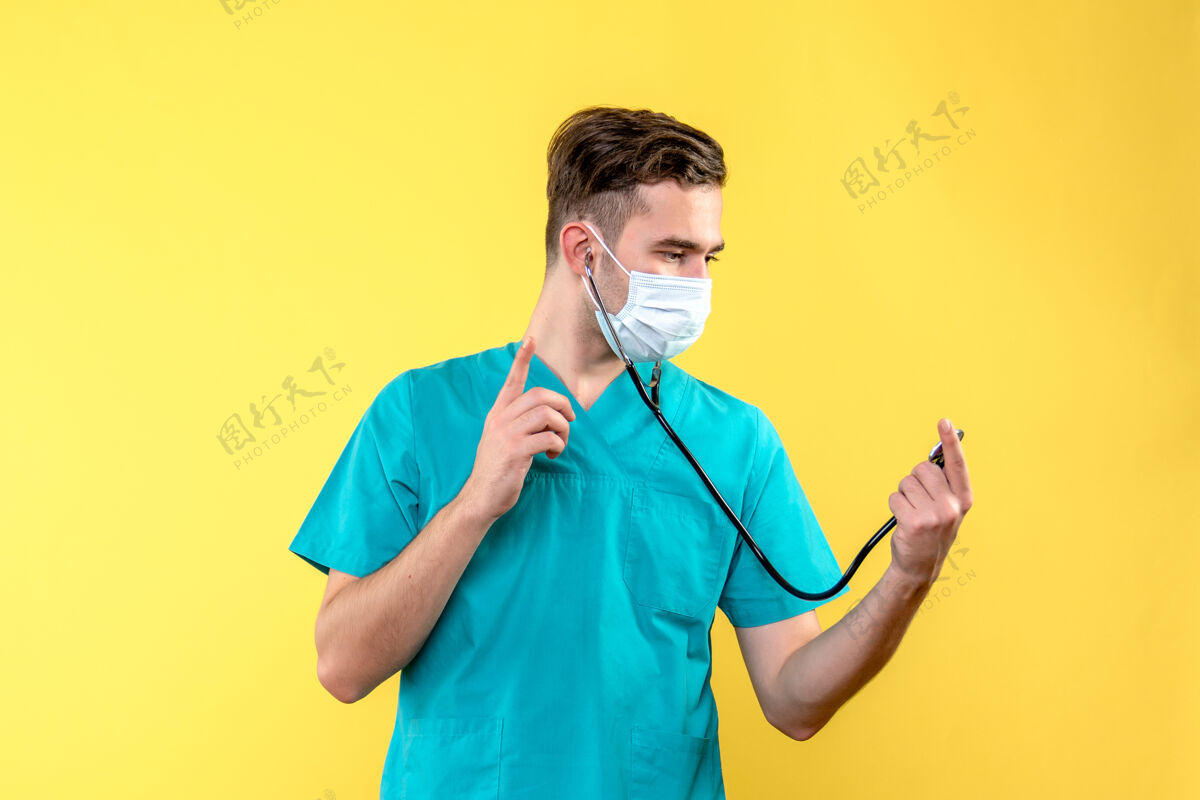 人黄色墙上带听诊器和面罩的男医生的正面图医疗器械肖像帅哥