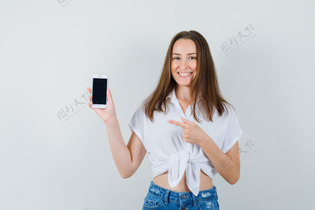 室内年轻的女士指着电话 穿着白衬衫 看起来很高兴前视图黑发电话成人