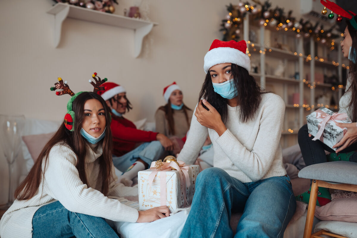 年戴着圣诞帽的多民族朋友们微笑着 手里拿着礼物对着镜头摆姿势在冠状病毒的限制下庆祝新年和圣诞节的概念检疫中的节日隔离房子圣诞老人