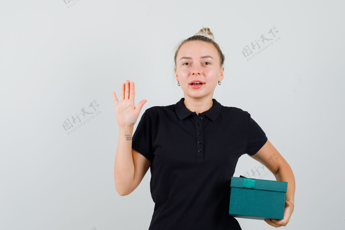 时尚金发女士拿着礼物盒 展示着身穿黑色t恤的手掌 看上去很欢快 正面视图魅力时尚金发