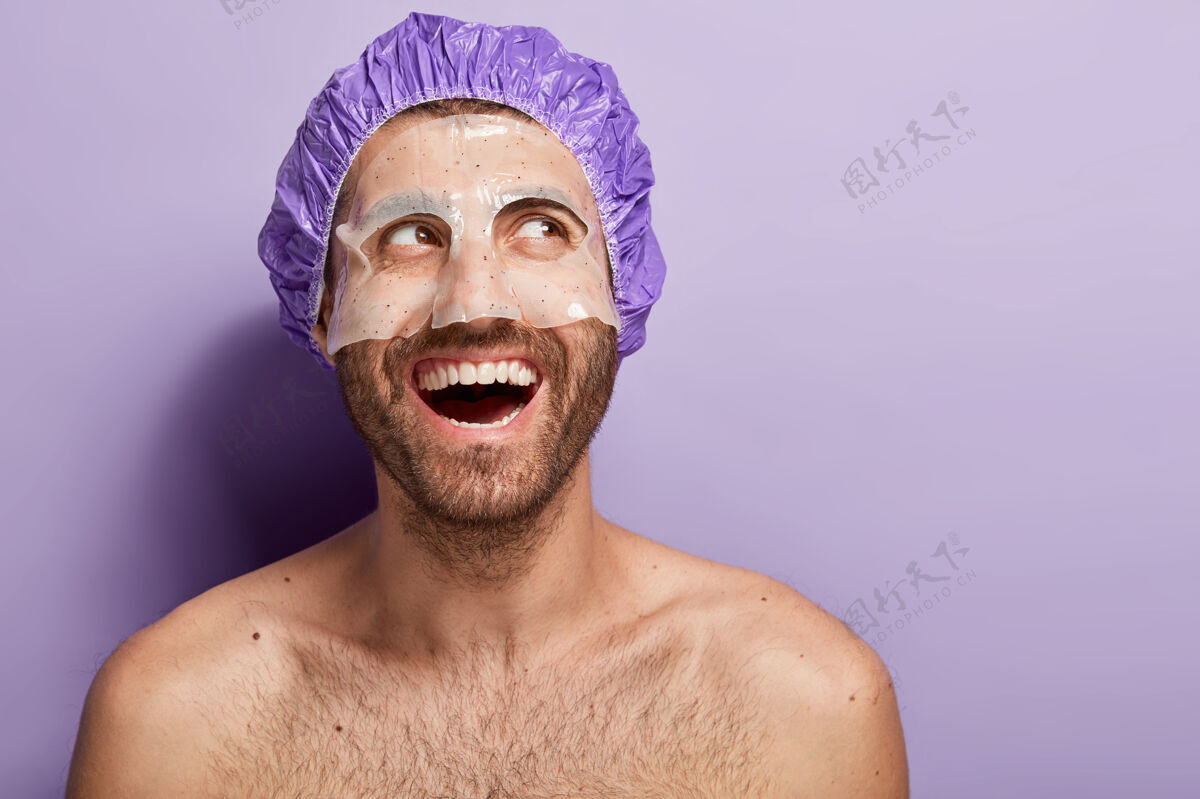 完美快乐积极的年轻人应用面膜 戴浴帽 积极笑 有裸身 黑鬃 享受SPA治疗赤裸上身姿势年轻