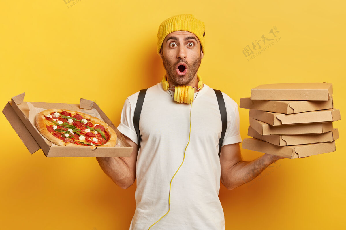 不健康披萨商拿着装有零食的纸箱 表情很严肃 戴着黄色帽子 穿着白色t恤 对某事印象深刻 有很多工作要做肖像小吃服务