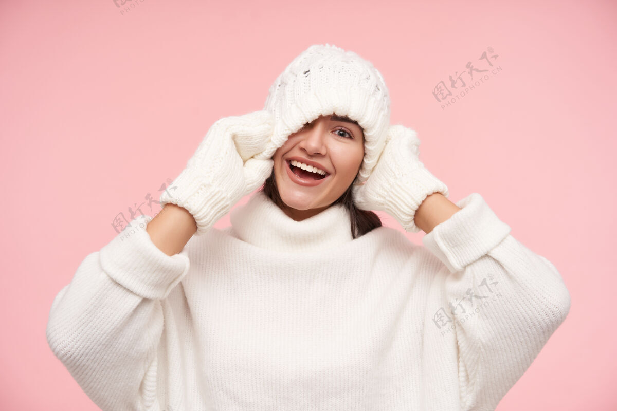 黑发摄影棚拍摄的年轻快乐的棕色头发的女人 自然化妆 开心地笑着 一边玩 举手向她的头 站在粉红色的墙上微笑手姿势